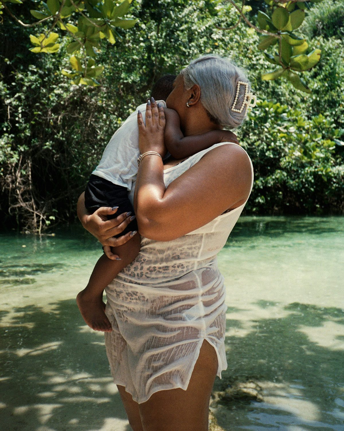 Photo by Kwabena Sekyi Appiah-nti of a person with grey hair standing in a natural pool while holding a child