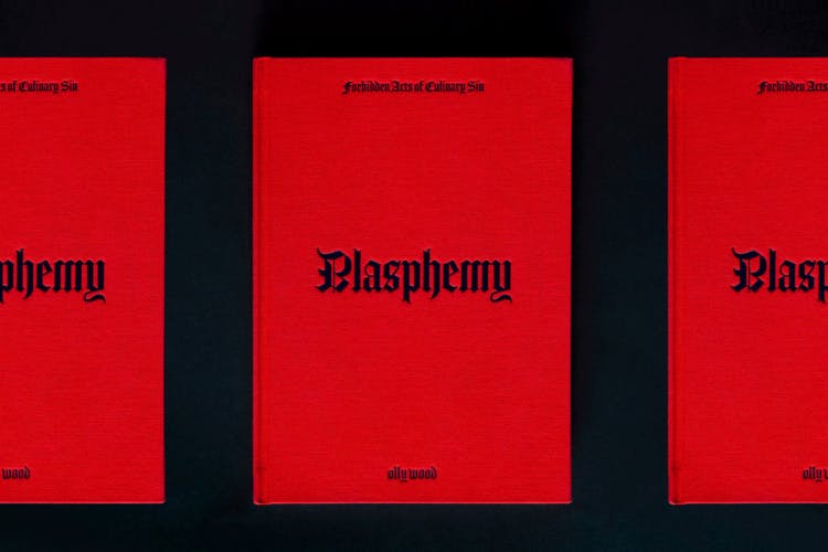 Row of three cookbooks with a read cover headlined 'blasphemy' in Gothic font
