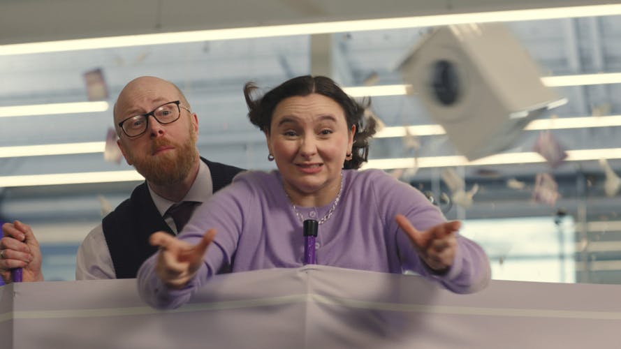 Two people behind a windbreaker with wind blowing into their faces and lifting a washing machine into the air, taken from Currys' Diversity in Advertising campaign