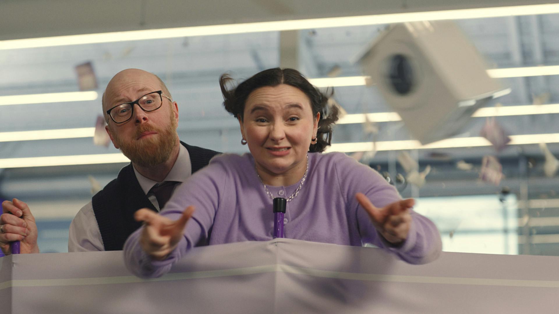 Two people behind a windbreaker with wind blowing into their faces and lifting a washing machine into the air, taken from Currys' Diversity in Advertising campaign