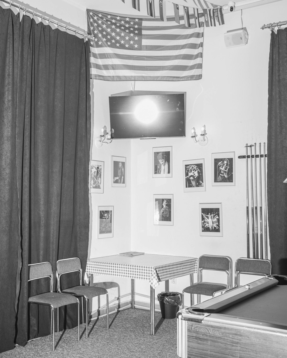 Black and white photo by Karol Szymkowiak showing a US flag in a room with a pool table, a table and chairs