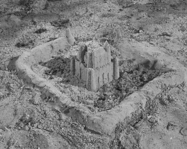 Black and white photo by Karol Szymkowiak showing a sand castle surrounded by a sand barrier
