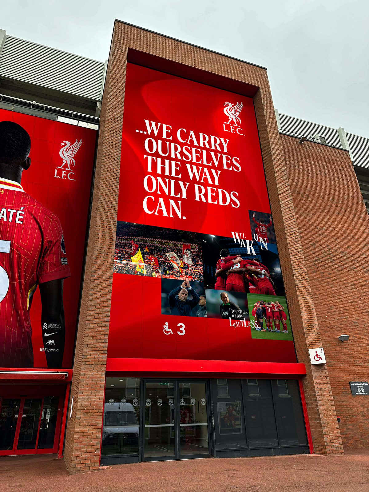 Liverpool branding shown on a stadium wrap outside Anfield that reads 'We carry ourselves the way only reds can'