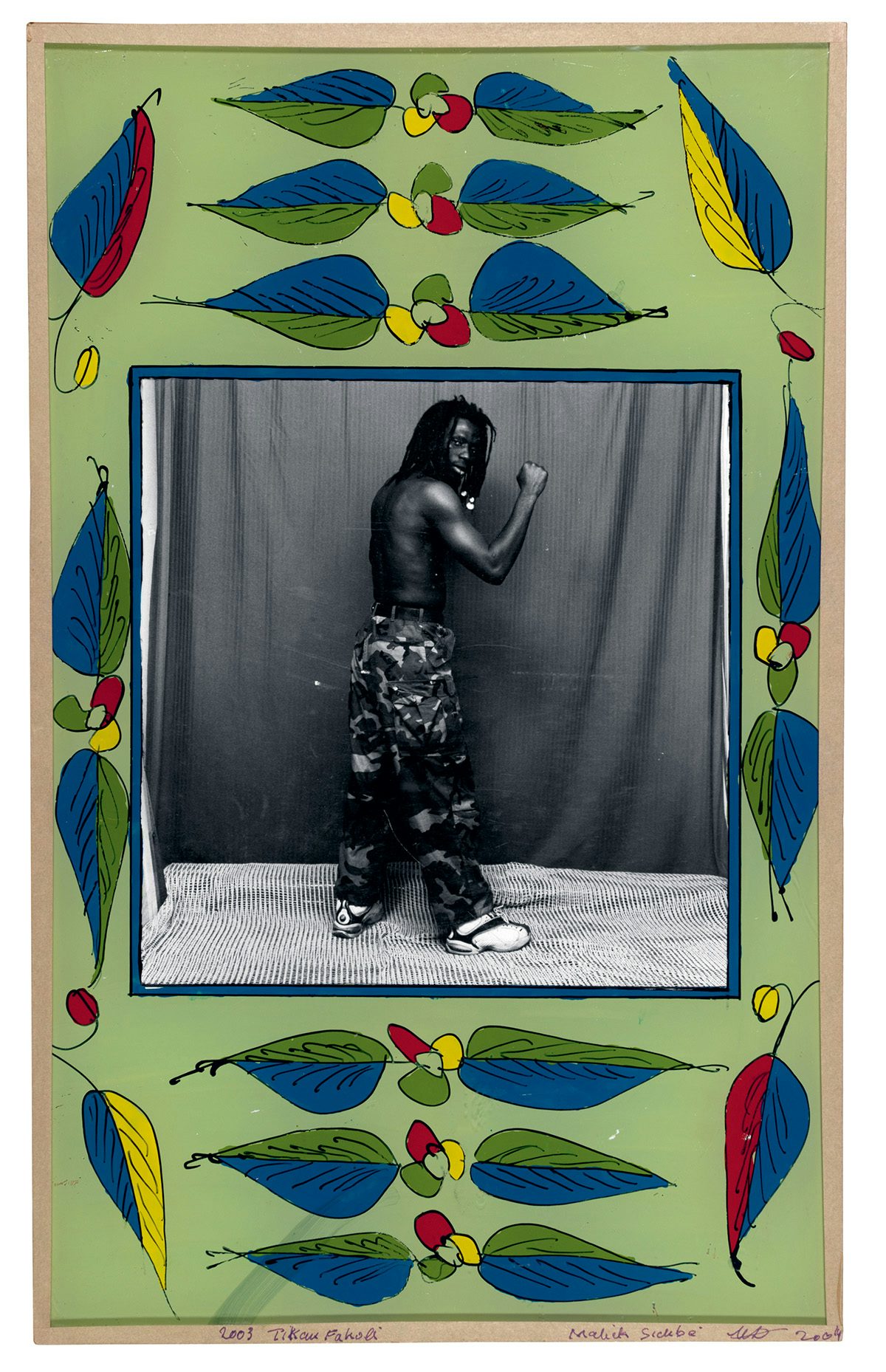 Black and white photo of a person wearing patterned trousers in a studio, which is bordered by a green painted frame