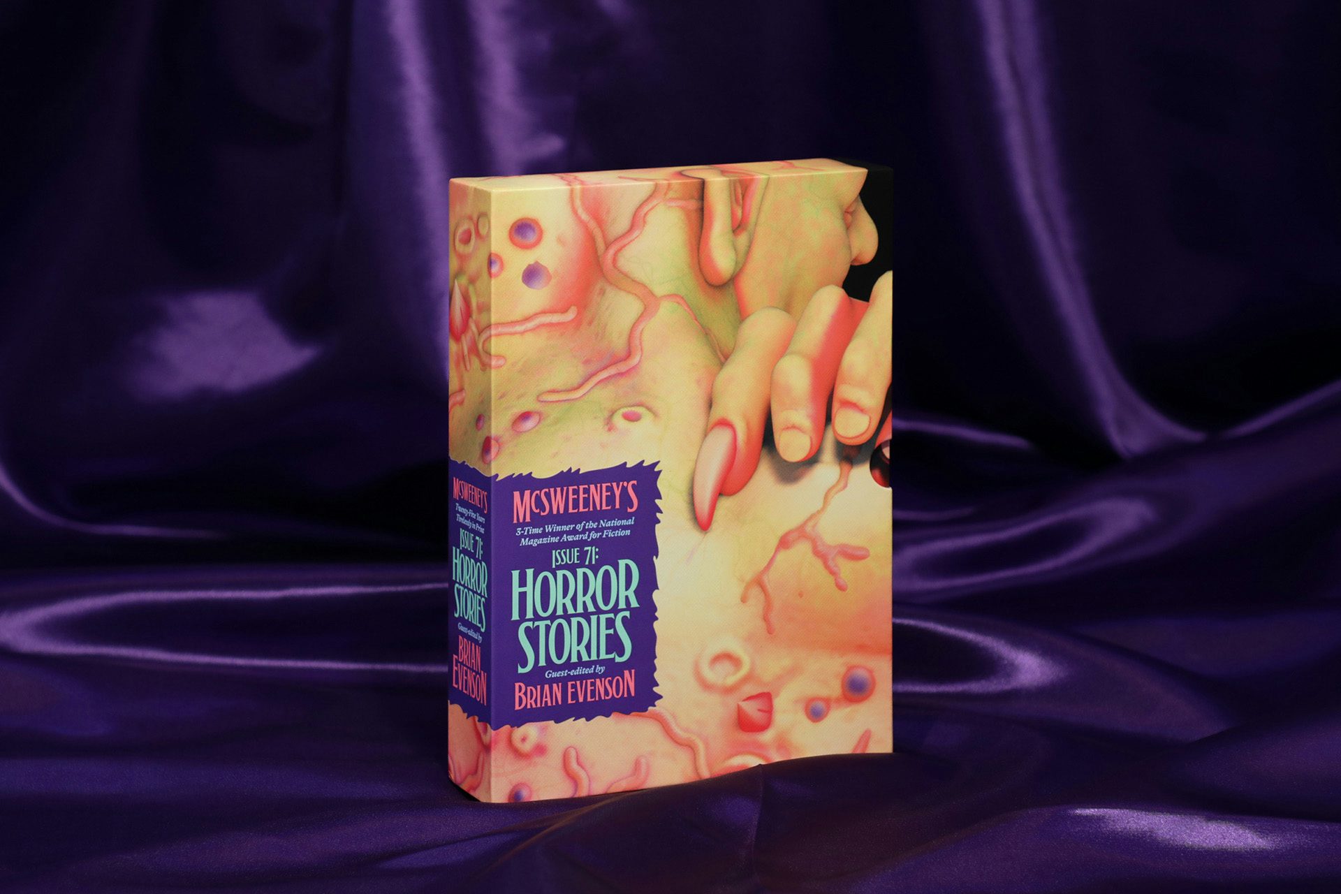 Photo showing the outer case for McSweeney's Issue 71 Horror featuring a horror illustration featuring pale flesh and finger nails, shown against a purple silk fabric backdrop