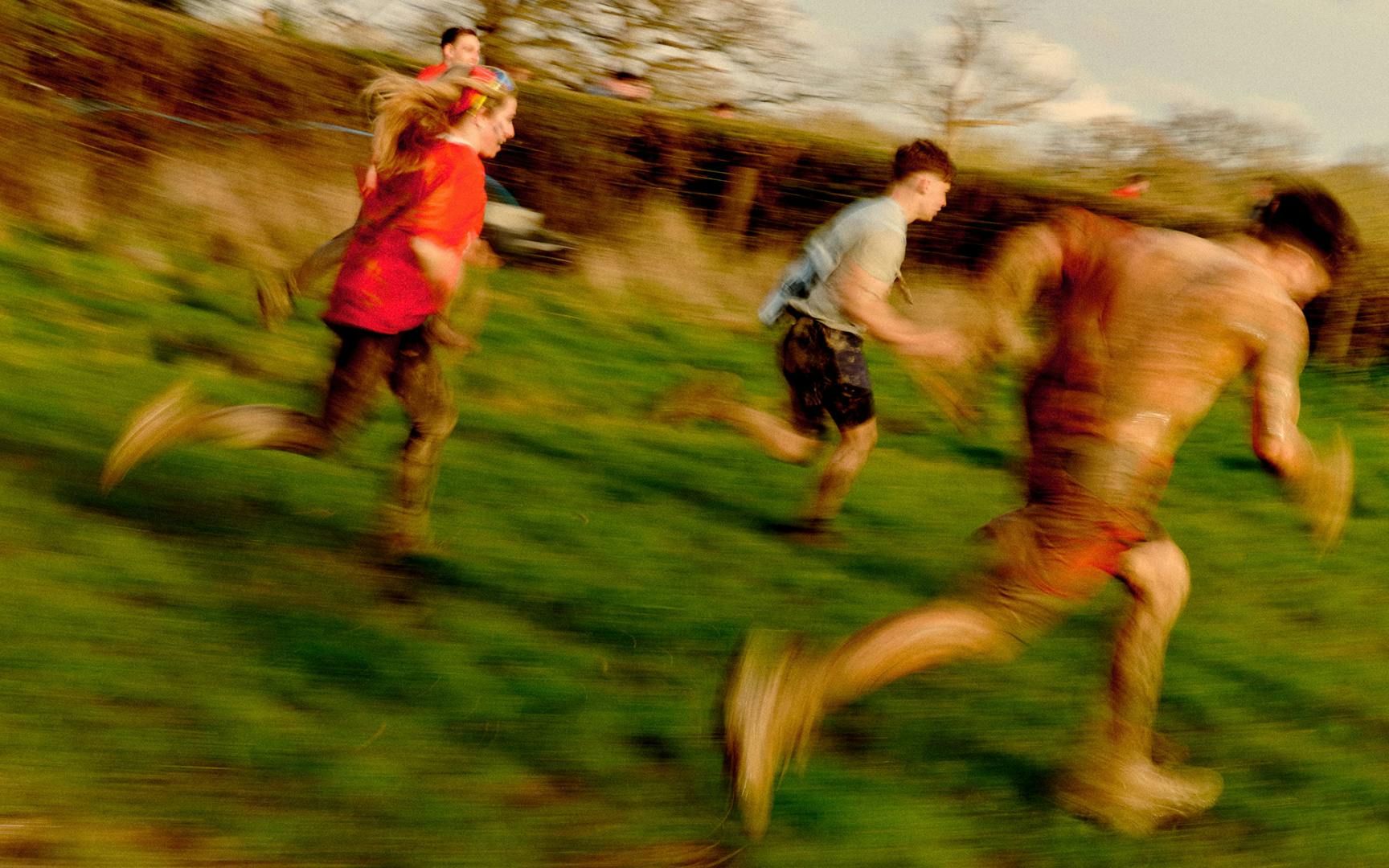 Young men in shorts and bare torso covered in mud while running through a field