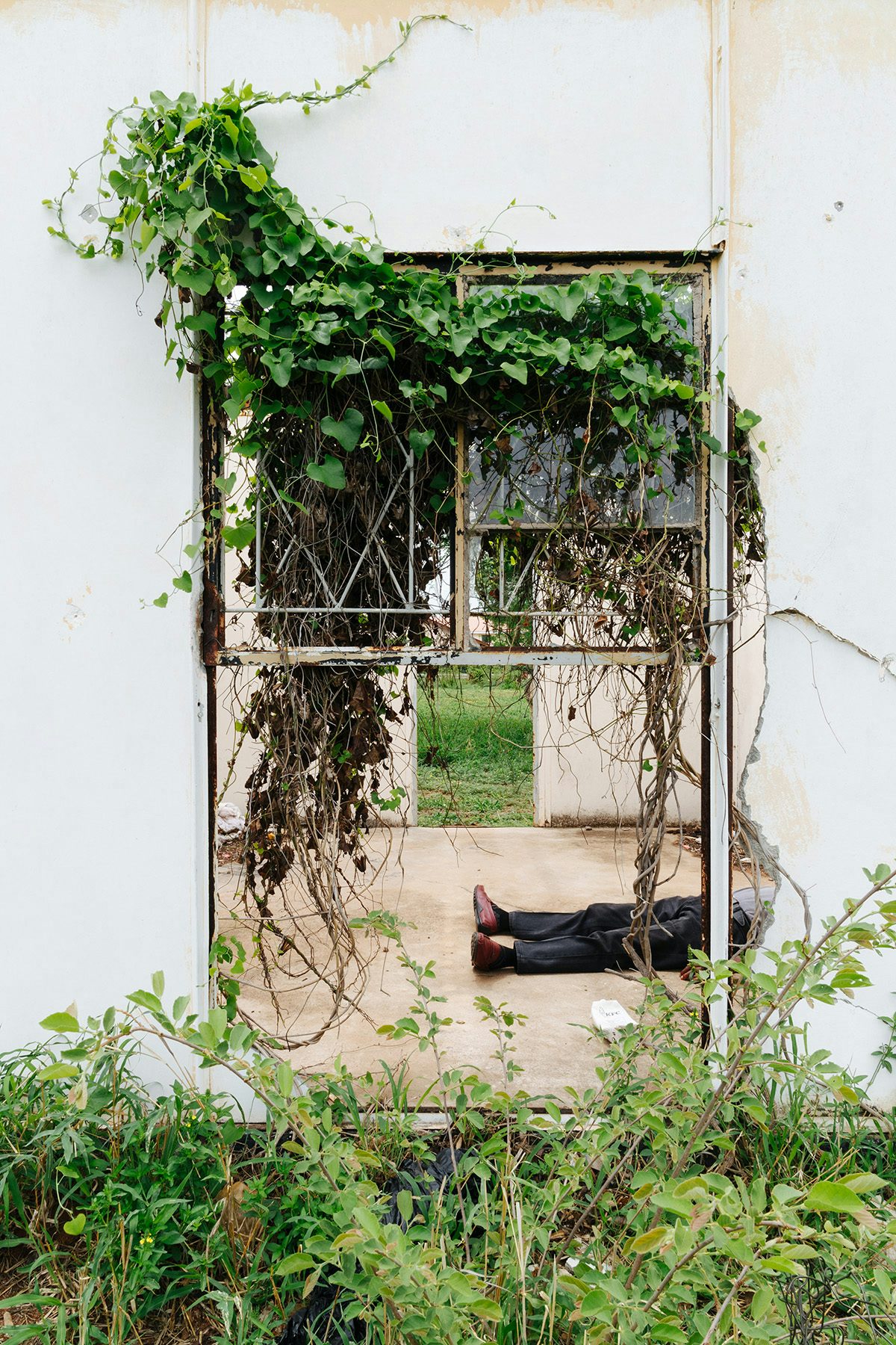 Photo by Thero Makepe of a person's legs on the ground visible through a doorway filled with overgrown ivy