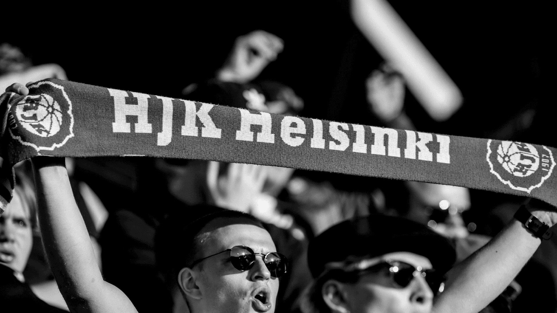 Black and white photo of a fan holding up a HJK Helsinki scarf